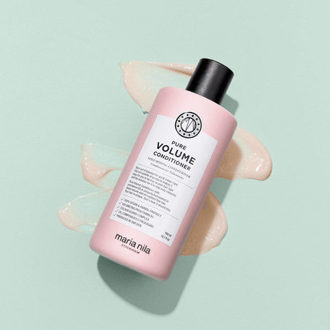 Revitalisant volume Pure Volume de Maria Nila pour cheveux, bouteille blanche avec étiquette colorée, appliqué sur des cheveux.