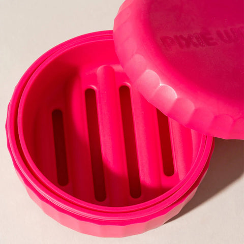 Étui de voyage rose pour shampoing en barre de la marque Pixie Woo, pratique pour emporter lors de déplacements capillaires.