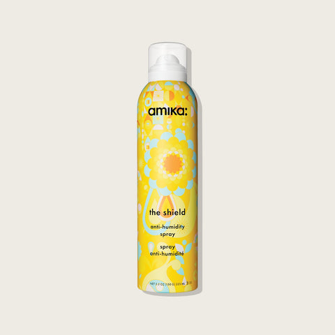 Spray anti-humidité pour cheveux Amika The Shield, flacon en spray avec étiquette bleue et logo Amika visible.