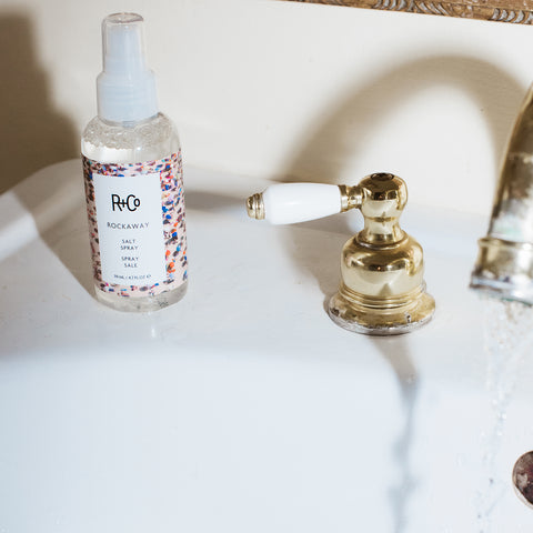 Spray salé R+Co Rockaway pour cheveux, flacon de 119 ml, avec spray blanc et logo de la marque.
