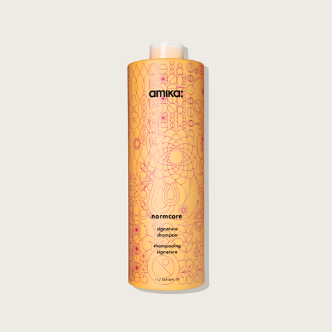 Shampooing signature Normcore de la marque Amika pour cheveux, bouteille blanche avec logo noir visible.