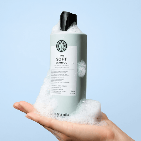 Shampooing assouplissant Maria Nila True Soft pour cheveux, bouteille blanche avec logo rose, tenue dans la main.